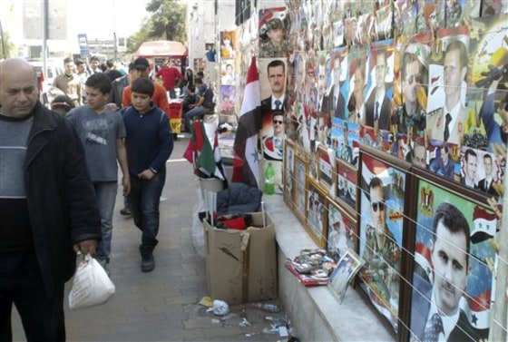 In this image&nbsp;from a mobile phone, people walk past pictures of Syrian President Bashar Assad in Damascus, Syria, on Wednesday. 